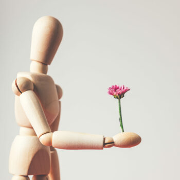 Wooden mannequin is holding tiny purple flower like chrysanthemum, concept of giving flower to lady, love, romance, dating
